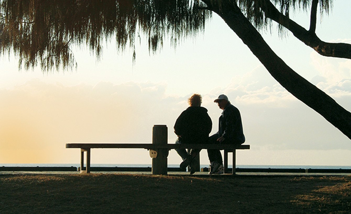Two people sitting on a bench in front of a bay shoreline